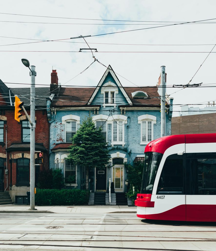 A red streetcar moves through the urban streets of Toronto, showcasing classic Victorian architecture.