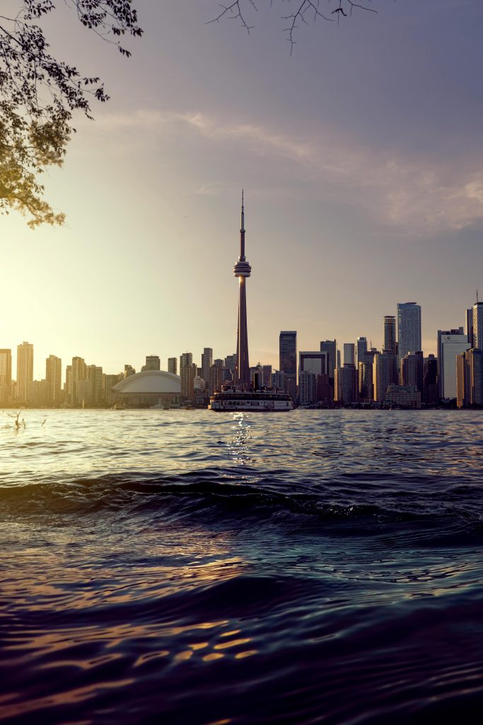 Captivating view of Toronto skyline with CN Tower at dusk, reflecting off serene waterfront.